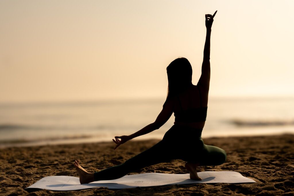 Yoga student in a standing pose facing the ocean during morning beach yoga in Hoi An.