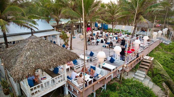 Aerial view of Shore Club's upper deck on An Bang Beach filled with guests enjoying live music, food, and cocktails under the late afternoon sun.